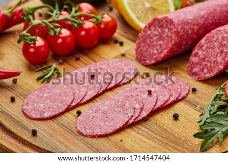 Traditional thinly sliced salami on a wooden cuttingboard  with spices, lettuce, avocado and tomatoes. Cold meat plate