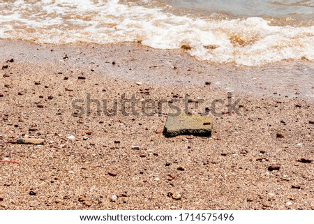 Some stones are on the sand at the beach and the water is moving.