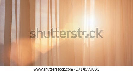 ray of sun lighting through transparent curtain on window into bedroom at evening summer time