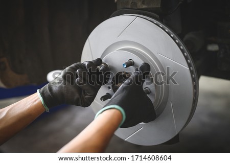 Car mechanic hands installing new six slot Disc Brake Rotor. Royalty-Free Stock Photo #1714608604