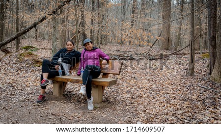 Two women sitting on a bench in the woods on a winter day with sneakers in Orange Country, North Carolina