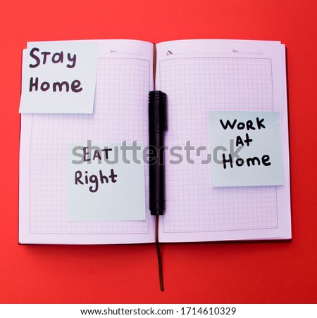 work notebook on a red table in the open position with inscriptions on the stickers "stay home, eat right, work at home"