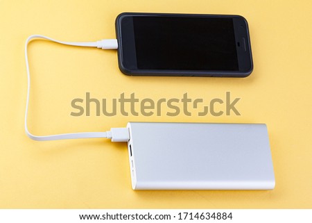Power bank charges your smartphone  on yellow background. Universal external battery for gadgets. Power bank for charging mobile devices . External battery for mobile devices.