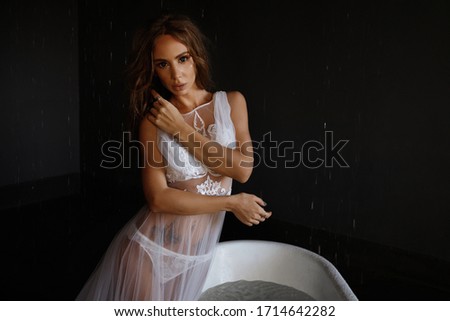 Beautiful model in a transparent peignoir in the bathroom. bathtub filled with water. portrait of a girl with makeup. morning of the bride