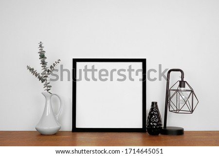 Mock up black square frame with home decor. Wooden shelf against a white wall. Copy space.