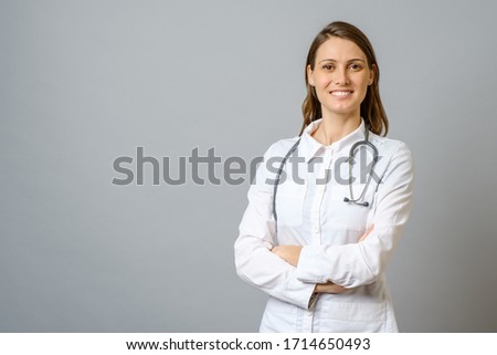 Smiling female doctor in lab coat with arms crossed over gray background