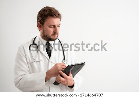 Portrait of male doctor with stethoscope in medical uniform takes notes, posing on a white isolated background