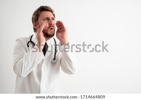 Portrait of male doctor with stethoscope in medical uniform shouting with her hands to her mouth posing on a white isolated background