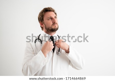 Portrait of male doctor with stethoscope in medical uniform arranges his collar posing on a white isolated background