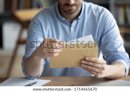 Focused businessman reading letter, looking at paper, holding envelope in hands close up, received news or important information, freelancer working with correspondence, sitting at work desk Royalty-Free Stock Photo #1714665670