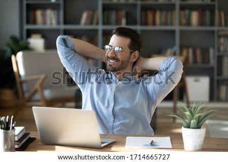 Smiling businessman freelancer wearing glasses leaning back in chair with hands behind head, happy satisfied young man dreaming about good future, new opportunities, visualizing success Royalty-Free Stock Photo #1714665727