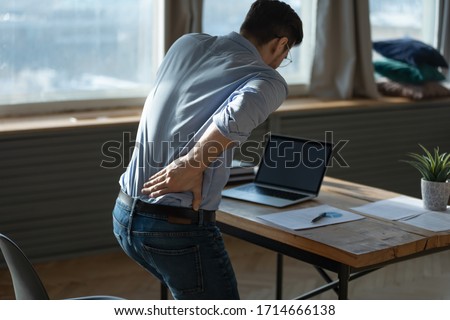 Rear view young man suffering from sudden backache, getting out of uncomfortable chair at workplace, touching lower back, unhealthy businessman student office worker feeling discomfort Royalty-Free Stock Photo #1714666138