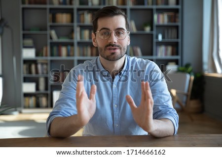 Head shot portrait confident businessman coach wearing glasses looking at camera and talking, mentor speaker holding online lesson, explaining, sitting at wooden work desk in modern cabinet Royalty-Free Stock Photo #1714666162