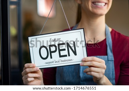 Small business owner smiling while turning the sign for the reopening of the place after the quarantine due to covid-19. Close up of woman’s hands holding sign now we are open support local business. Royalty-Free Stock Photo #1714676551