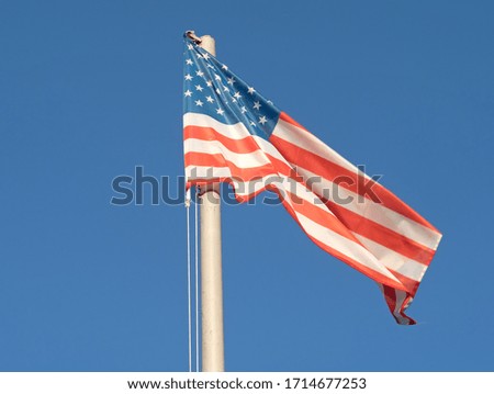 American flag - star and stripes floating over a cloudy blue sky
