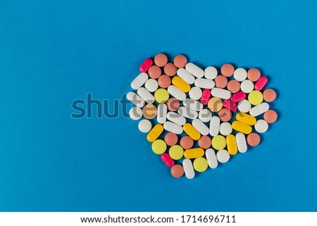 Close-up picture of different pills and tablets folded in shape of heart on blue background. Many pills and tablets with space for text. Pharmaceutical picture. Nice wallpaper