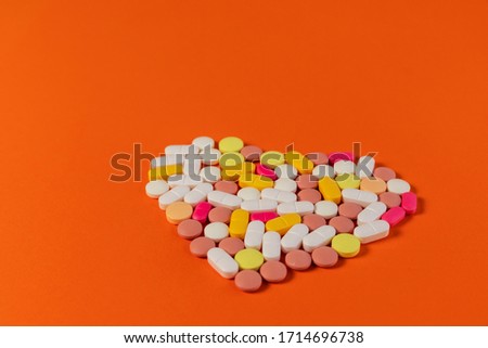 Many different pills and tablets folded in shape of heart on orange background. Many pills and tablets with space for text. New image. Pharmaceutical pills. Closeup picture of heart of pills