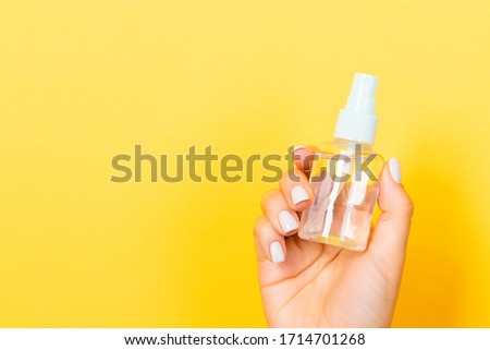 Female hand holding a spray of cosmetic product at yellow background with empty space for your design.