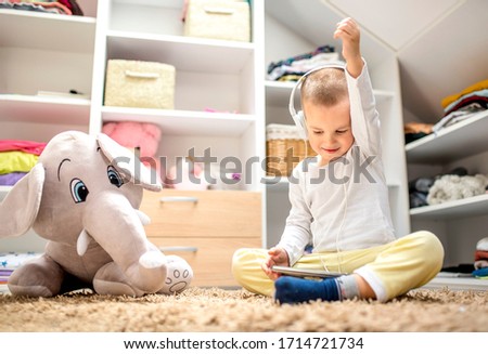 Adorable little boy with headphones sitting on the floor with favorite plush toy and playing games on tablet