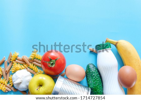 Food supplies , crisis food stock for quarantine isolation period on blue background. Pasta,tomato,canned food, cucumber, apple, banana, garlic.