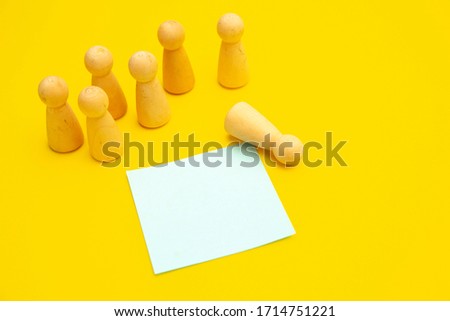 Group of people and a one separate person. Wooden pawns are stanging over isolated yellow background near blue sticky note for writing