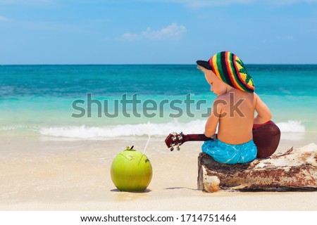 Little baby in rasta hat play reggae music on Hawaiian ukulele, enjoy relaxing on ocean beach. Kids healthy lifestyle. Family summer holiday. Activity on tropical Jamaica and Caribbean island travel.