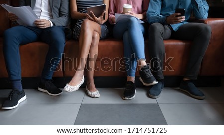 Close up of diverse multiethnic young people sit on couch waiting for job interview in office, multiracial colleagues coworkers seated on sofa in queue preparing for work hiring, recruitment concept