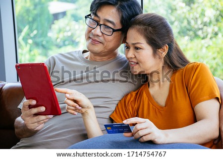 Happy senior Asian couple are looking at their tablet with a credit card ready to pay at the living room in their home