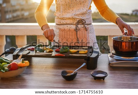 Young woman grill vegetables while preparing dinner in patio terrace outdoor during isolation quarantine - Food, healthy lifestyle and vegetarian concept - Focus on left hand