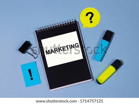 text Marketing on black notepad with clips, markers, sticker on blue table. Business concept