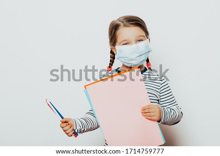 child little girl in medical mask is sitting at home in quarantine. education. kid with pencils and colored paper. Entertainment for the  children during quarantine. Self isolation.  