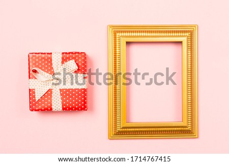 Golden frame empty blank picture and red gift box on light pink background . 