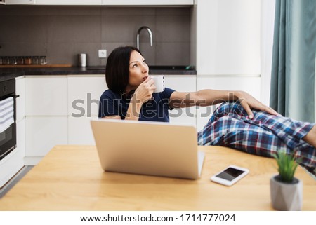 Attractive and happy middle age female freelancer is working and smiling at her home. Modern kitchen in background. Freelancing job concept.