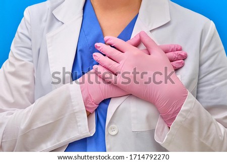 The doctor's hands are folded over his heart. Nurse in protective pink medical gloves, close-up. Concept stay home until the end of isolation due to coronavirus, blue background.
