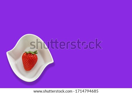 Strawberry in a white bowl on a neon purple color background  There is enough space in the photo for your use.