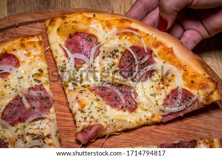 

Hand holding Pepperoni pizza in Brazil is called Pizza de calabresa. close up