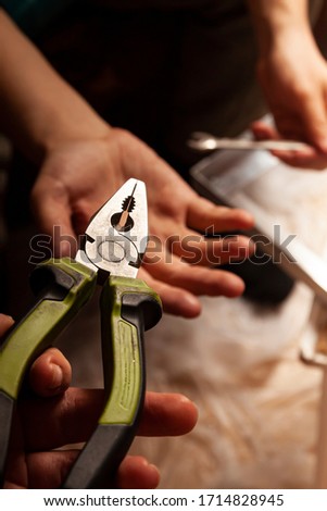 The hand of the assistant passes to the master, who repairs the iron case of the pliers. A man at home pursues his DIY hobby.