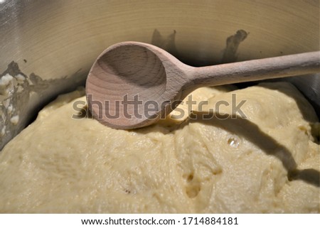 Butter yeast dough (with bubbles) and textured wooden spoon in a metal bowl