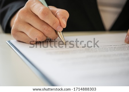 Closeup view of hand of a businesswoman or lawyer signing document with a pen.
