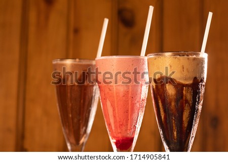 Three glasses of various milkshakes (chocolate, strawberry and vanilla) on wood background