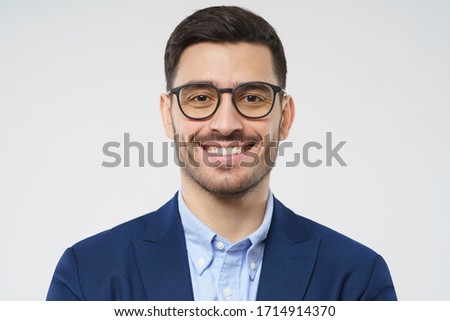 Close-up headshot of young businessman wearing glasses and smart casual suit, smiling at camera, isolated on gray background Royalty-Free Stock Photo #1714914370