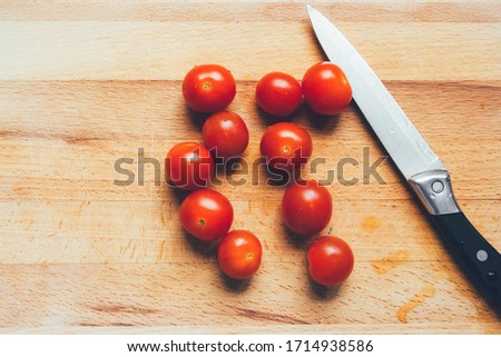 Vibrant cherry tomato and kitchen knife on a wooden chopping board lying on gray linen tablecloth. Stylish graceful picture. Photos for food recipes.Knife and cherry tomatoes lie on a wooden board.