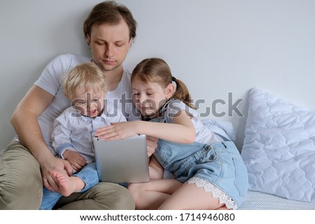 A happy family spends time at home. A father with two children watches cartoons and plays games on a laptop. Father with daughter and son hugs