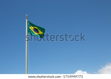 Flag of Brazil weathered with two faces and blue sky with white clouds