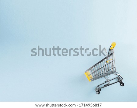 A yellow empty mini shopping cart on pastel blue background
