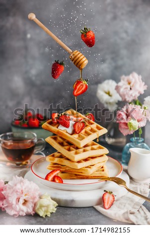 Plate of waffles with fresh strawberries and honey on gray background. Food levitation. Dessert with cup of tea. Royalty-Free Stock Photo #1714982155