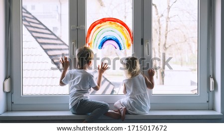 Little children on background of painting rainbow on window. Photo of kids leisure at home. Positive visual support during quarantine Pandemic Coronavirus Covid-19 at home. Family background