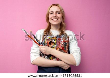 Young happy girl artist holds drawing equipment and smiles on a pink background, the work of the artist
