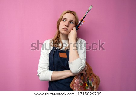 Young unhappy girl artist holds drawing equipment and is sad on a pink background, lack of inspiration, creative crisis