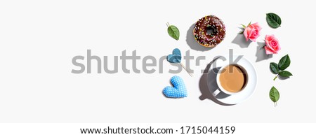 A cup of coffee with pink roses and a chocolate donut